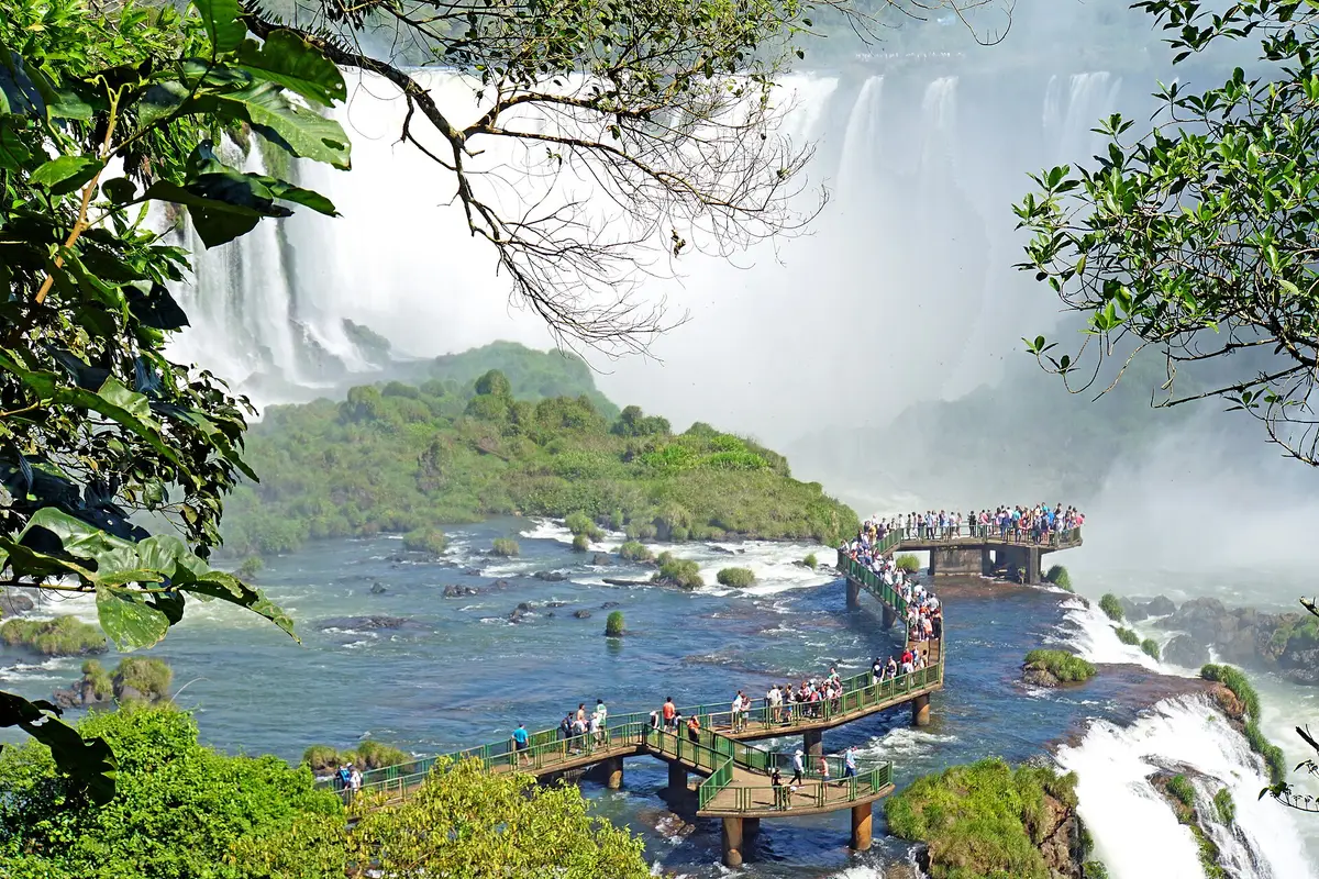 Visitors on the walkway over the river, with the falls and green forest behind